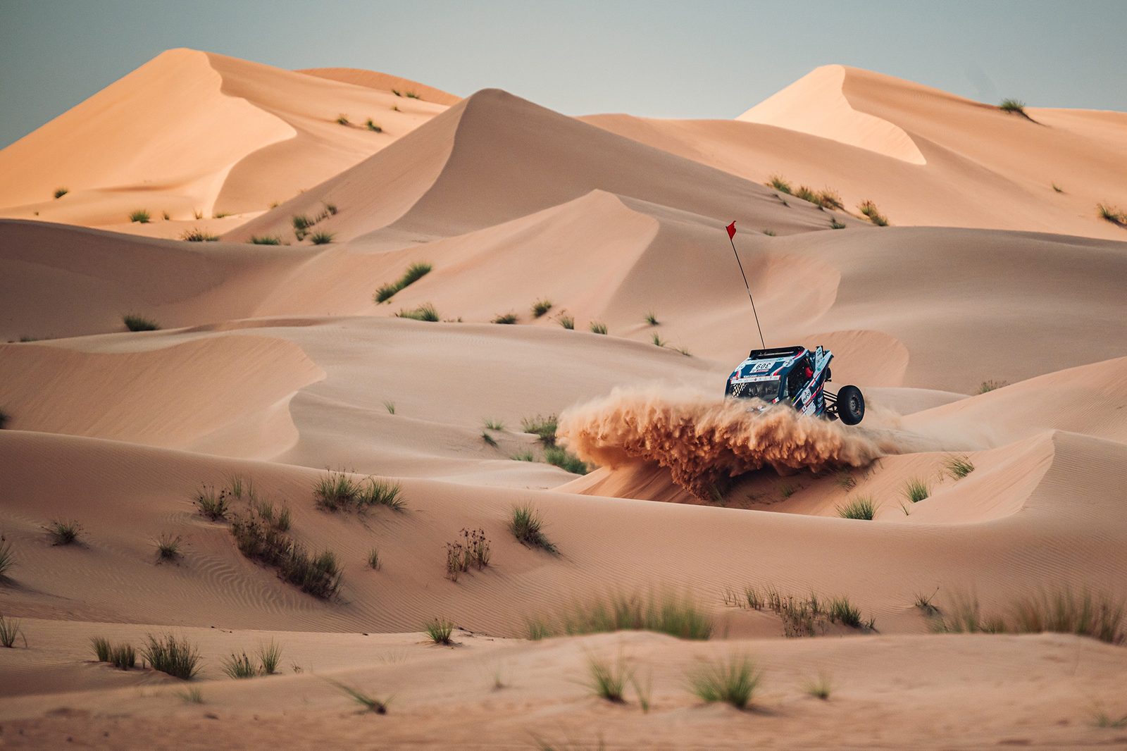 Rally car crossing wide sand dunes under a clear sky at the Dubai International Baja