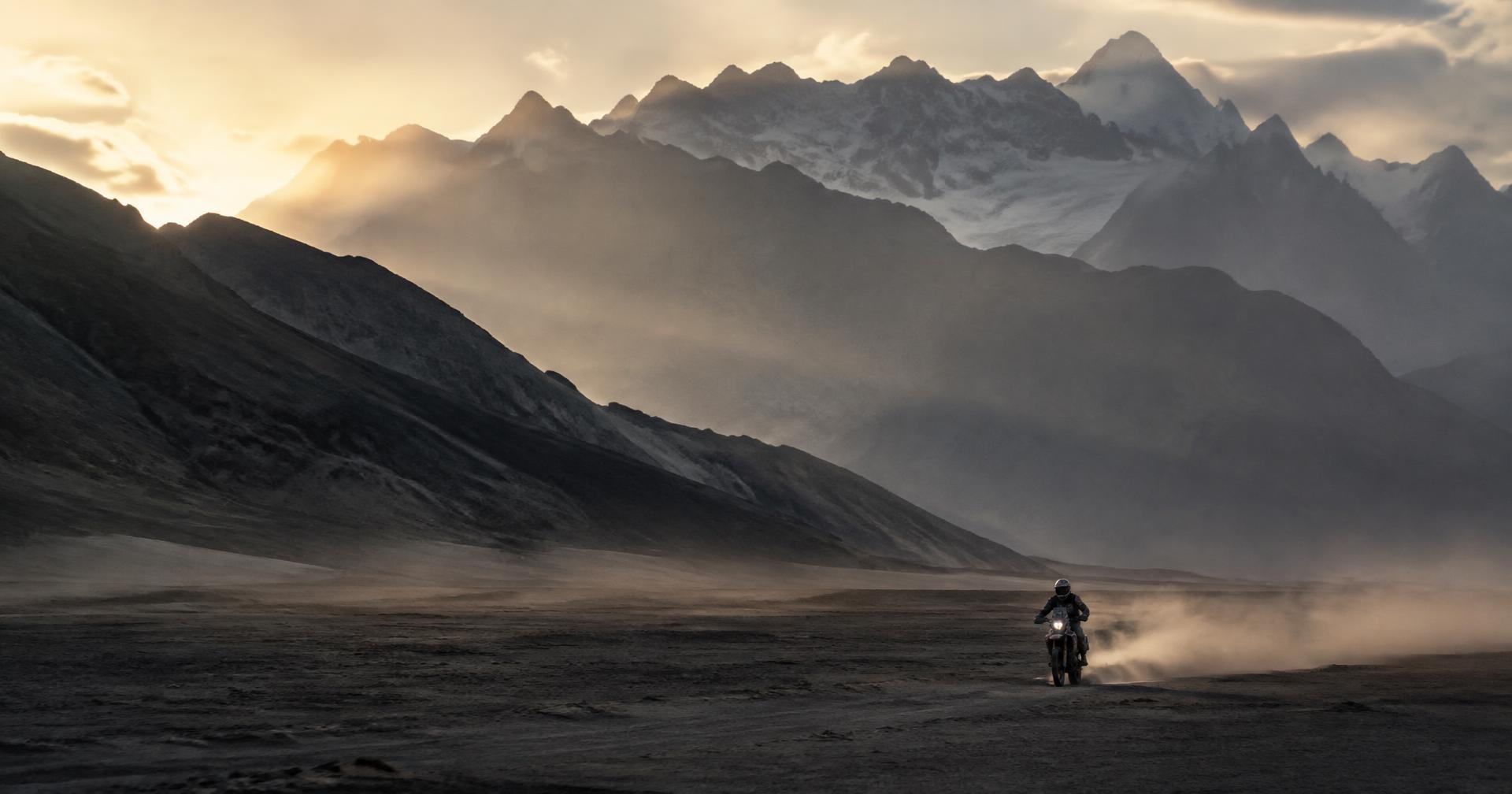 Lone rally rider crossing a vast dusty plain at dawn