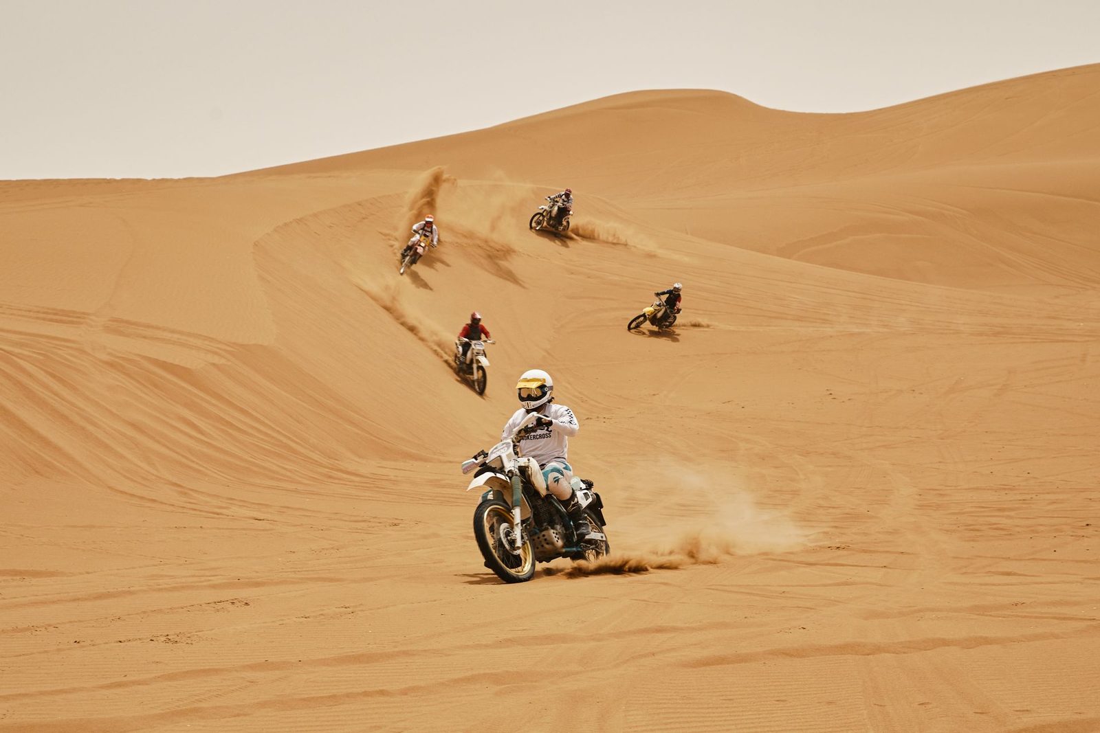 Riders on vintage-style rally motorcycles crossing soft dunes during Sandraiders in Tunisia
